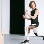 A young woman performing lunges with dumbbells in a modern indoor gym setting.